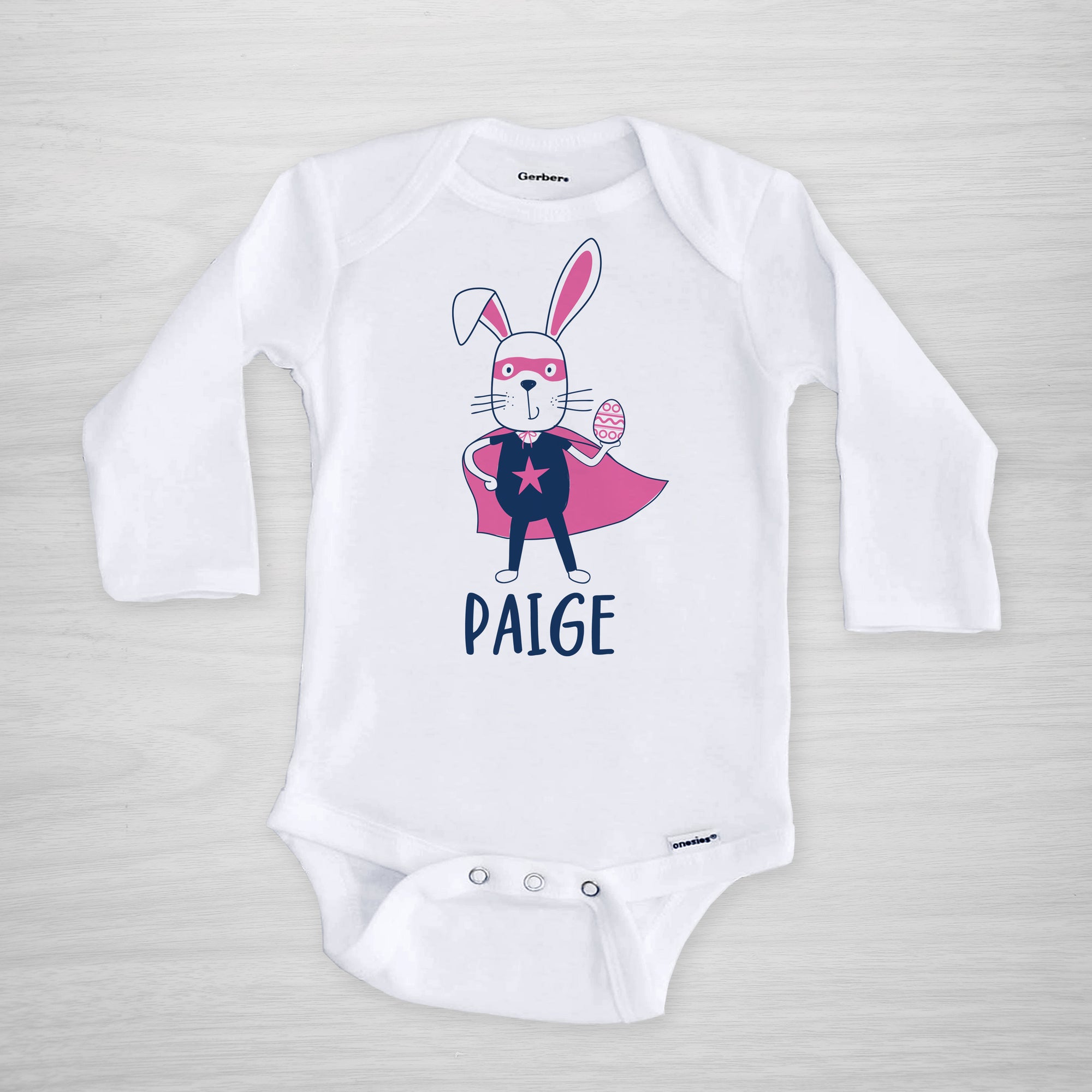 Superhero Easter Bunny with a cape, mask, and egg on this personalized Gerber Onesie®, long sleeved pink