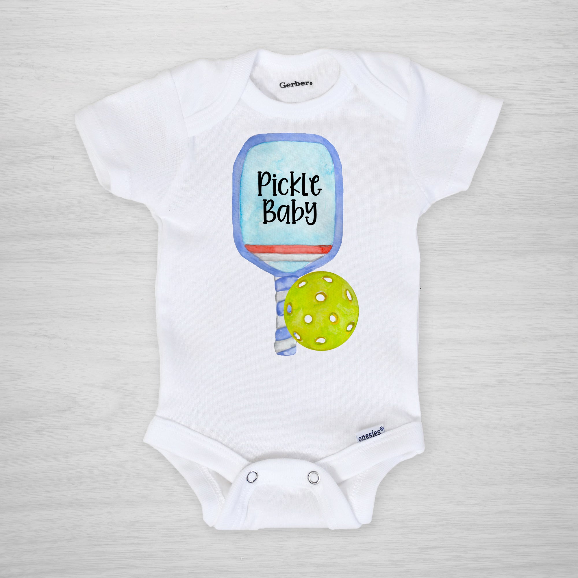 Pickleball Gerber Onesie® with a blue paddle. You can leave a note and specify team colors for the text. Otherwise, the print will be black as shown. Makes a great shower gift for the new pickle baby