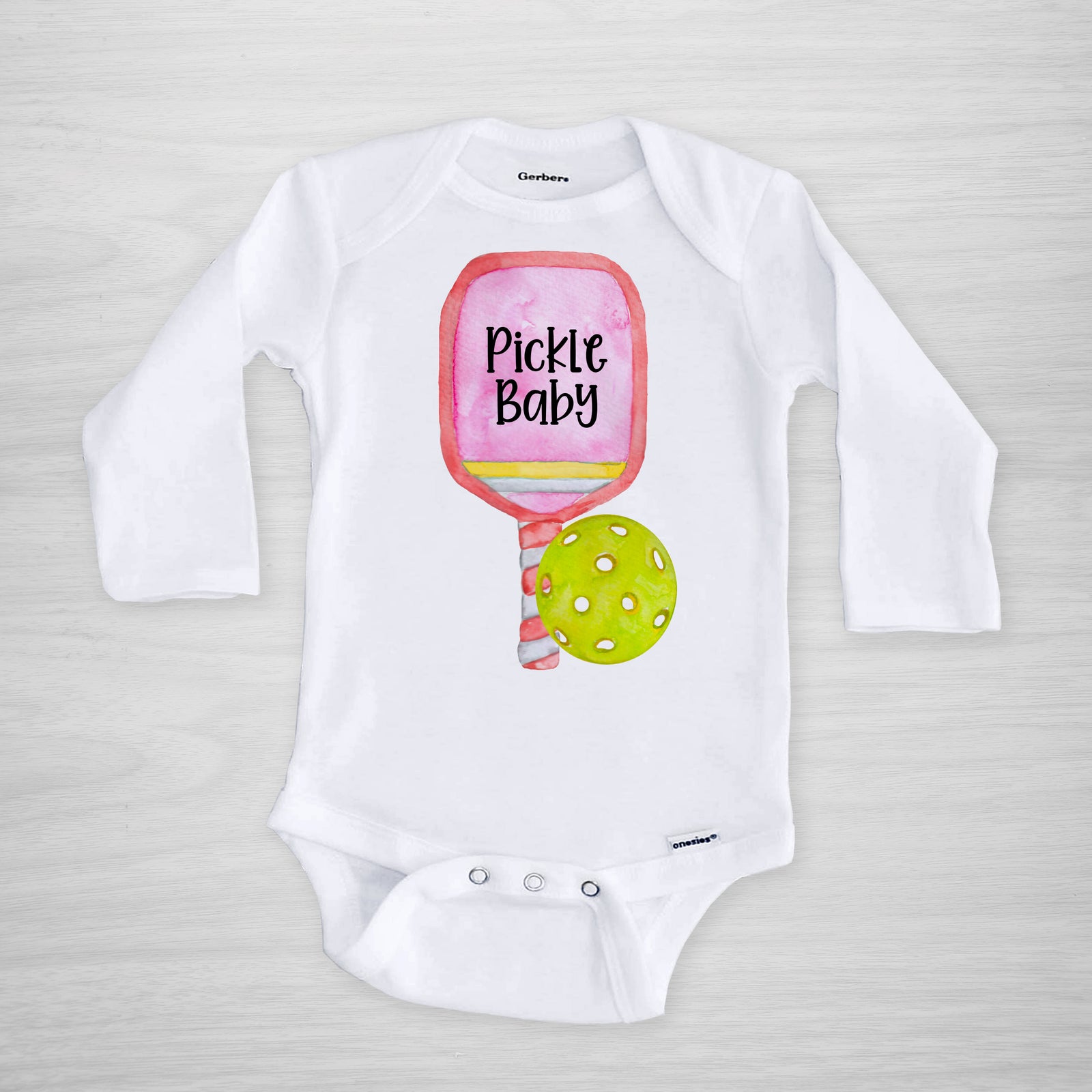 Pickleball Gerber Onesie® with a pink paddle. You can leave a note and specify team colors for the text. Otherwise, the print will be black as shown. Makes a great shower gift for the new pickle baby