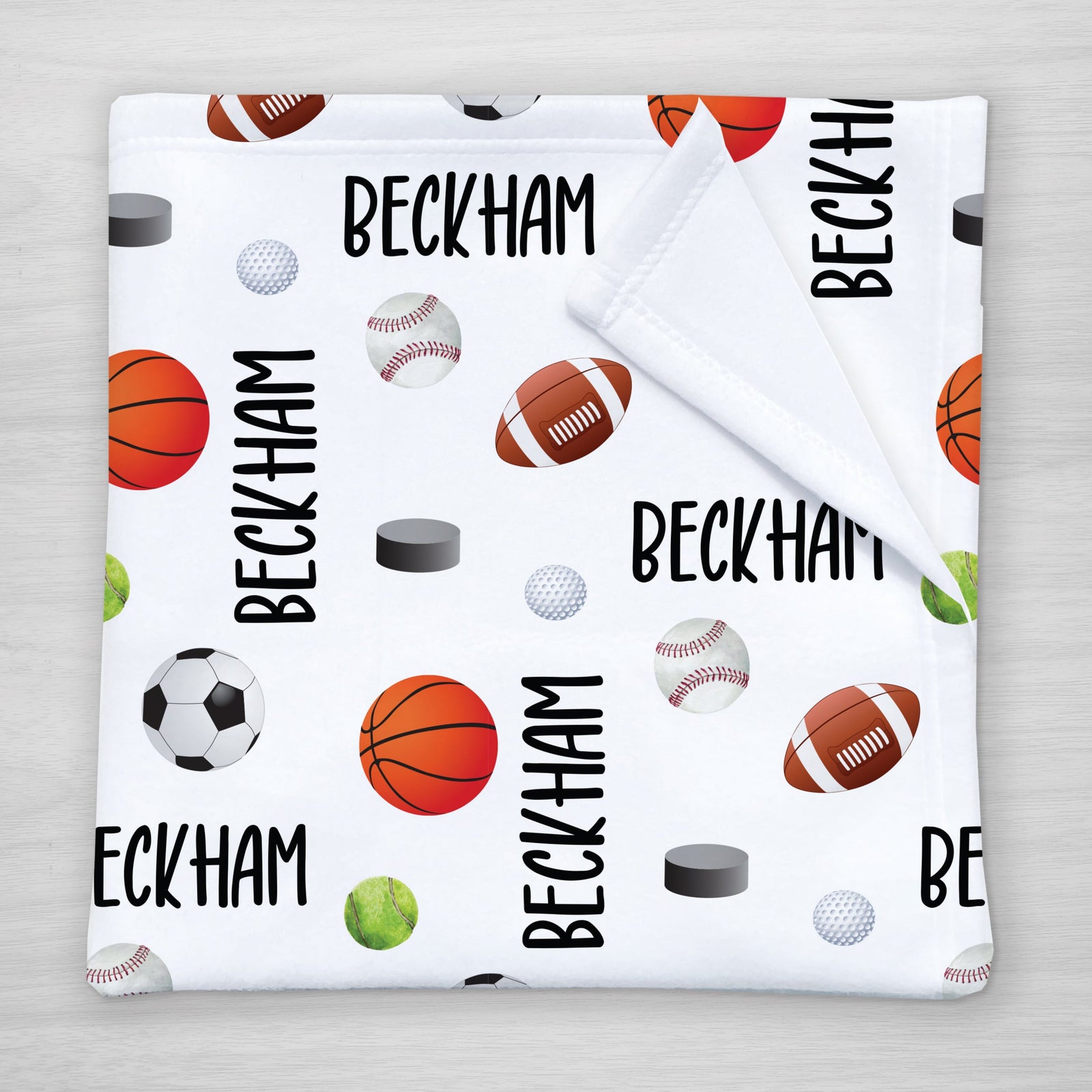 A personalized blanket with a sports theme, featuring your child's name and various sports icons such as a football, basketball, hockey puck, tennis ball, and baseball on a white background.