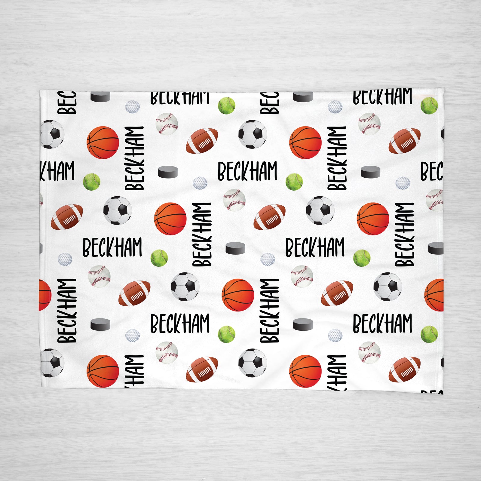 A personalized blanket with a sports theme, featuring your child's name and various sports icons such as a football, basketball, hockey puck, tennis ball, and baseball on a white background.