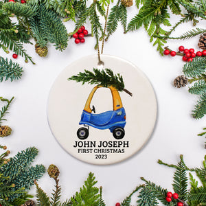 A first Christmas ornament with a blue and yellow toy car and tree. It is round ceramic and can be personalized and include the year.