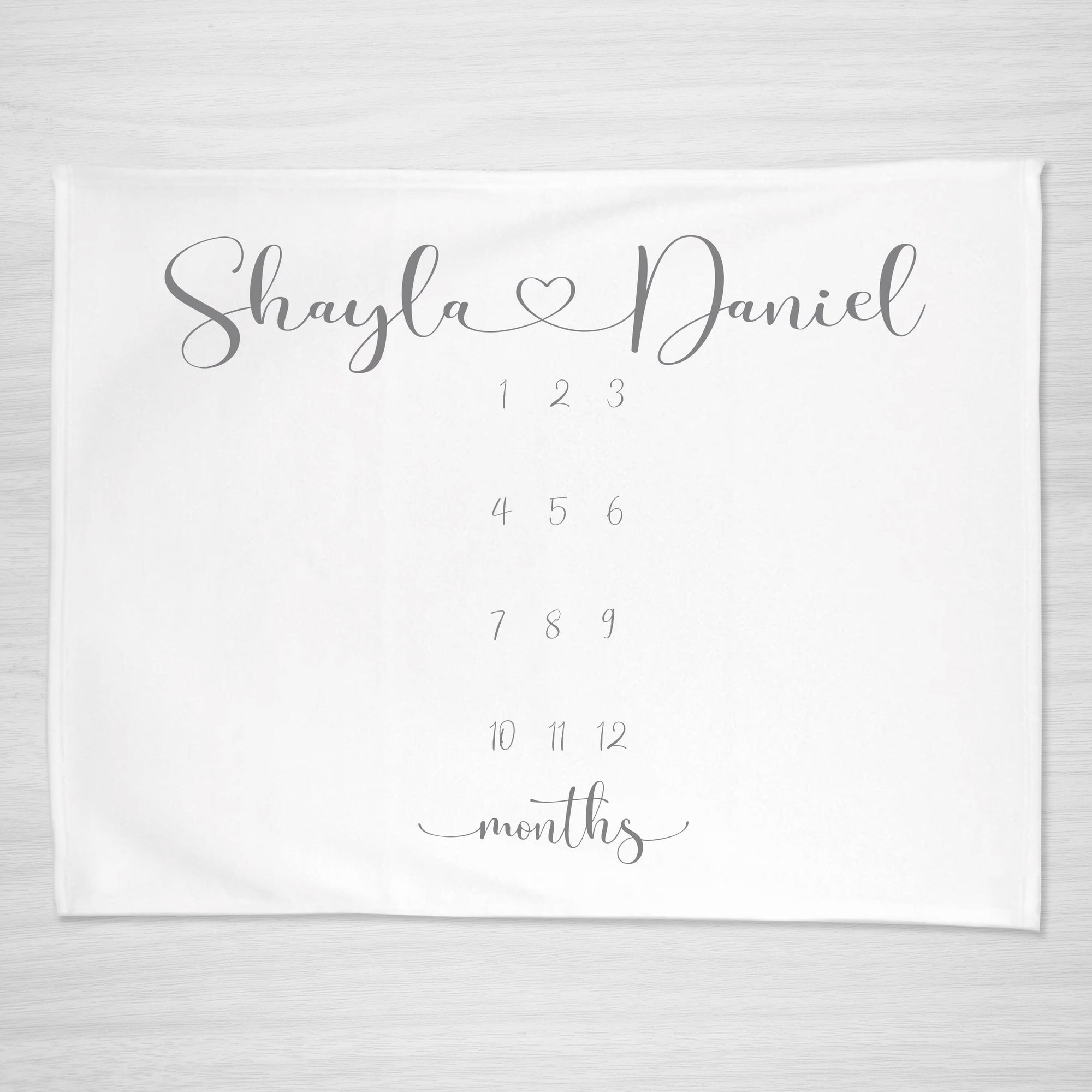 Twin milestone blanket featuring an elegant script font with a heart joining the babies names. 