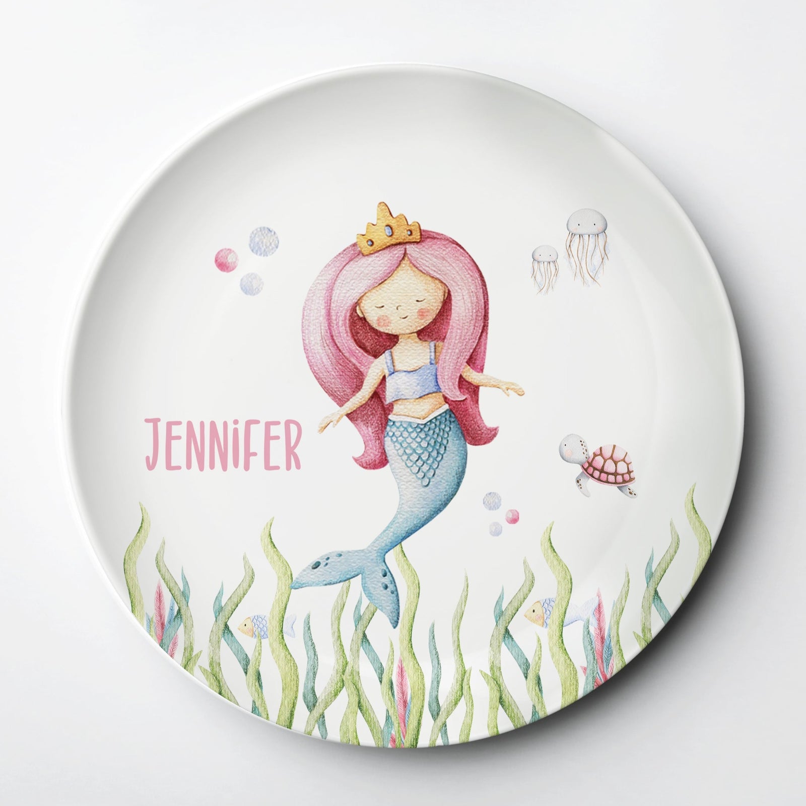 Fun mermaid with pink hair floating in the center of the plate above a kelp forest.  Turtle, jellyfish and a few fish swimming complete the scene for all your mermaid loving kids!  ThermoSāf® reusable plate that is dishwasher, oven and microwave safe! Pipsy.com