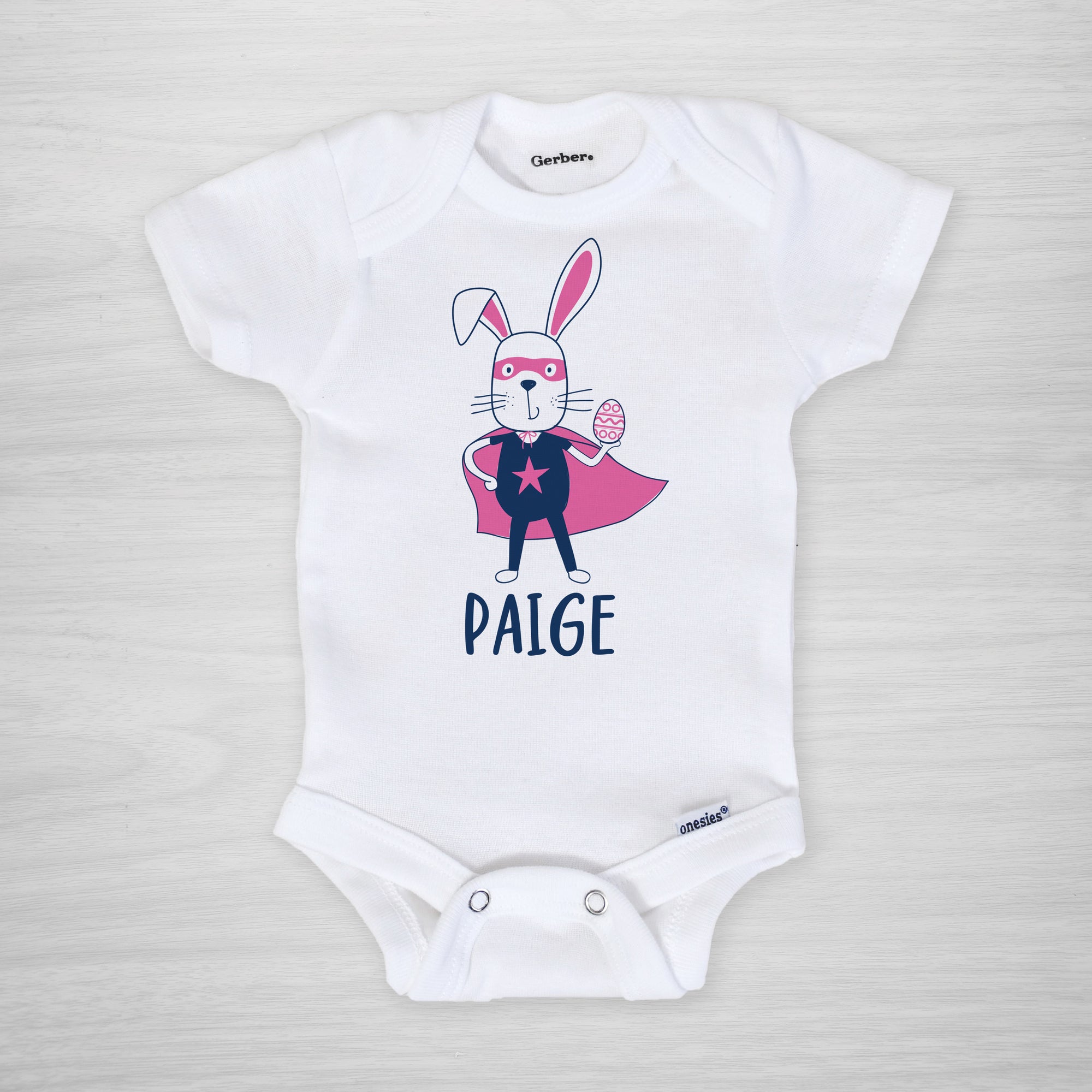 Superhero Easter Bunny with a cape, mask, and egg on this personalized Gerber Onesie®, short sleeved pink